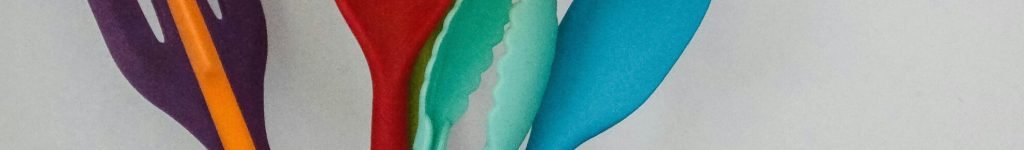 Colorful kitchen utensils in a glass jar against a neutral background.